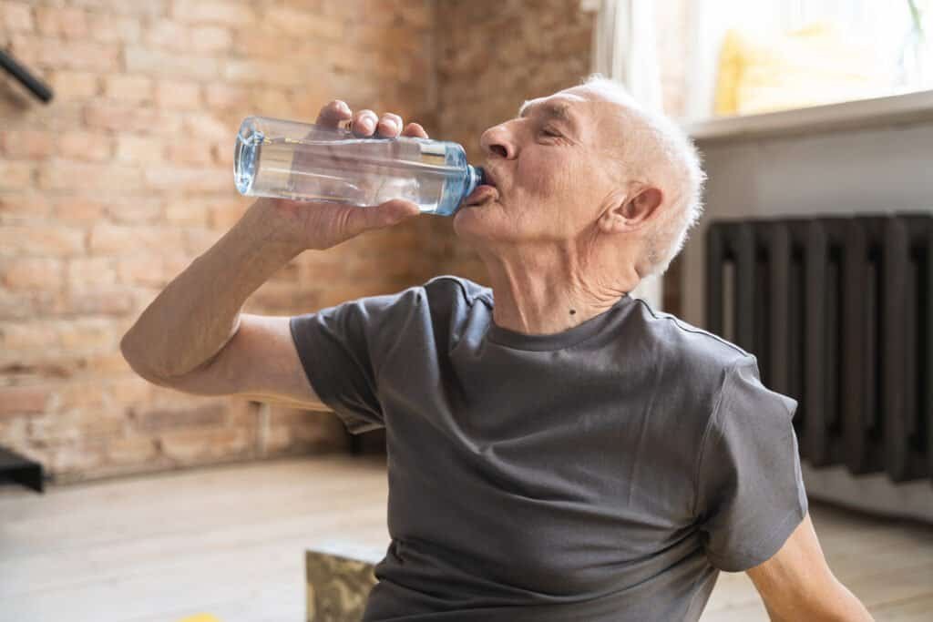f active elderly man drinking water after fitness workout at home