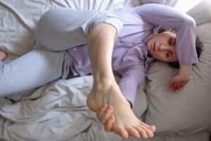 Caucasian woman looking on her hairy leg resting on bed at home. She can not do depilation in quarantine. Top view.