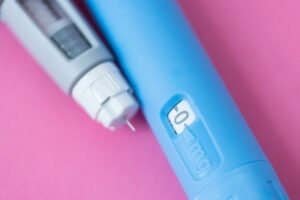 Insulin injection pens placed on pink surface. Medical tools for diabetes management. Close-up of healthcare equipment used for hormone delivery and blood sugar control.