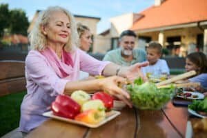 Senior woman is serving salad to her family during a lunch in the backyard of their home. The family is gathered around a table, enjoying each other's company