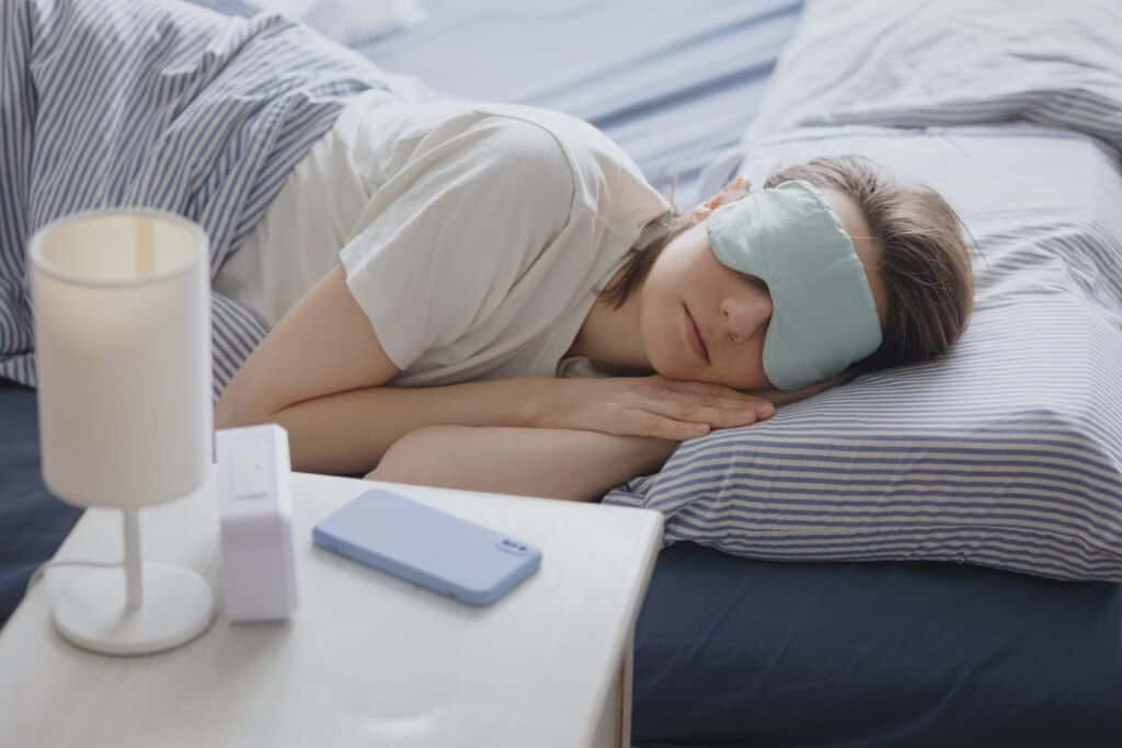 woman in bed with a sleep mask wakes up and turns off the alarm. a clock