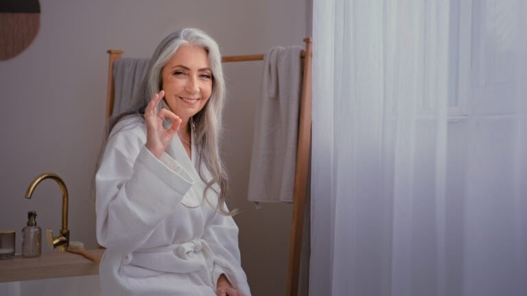 Aged senior mature lady Caucasian old gray-haired woman female in bathrobe in bathroom after washing beauty procedure showing ok recommend gesture happy satisfied with anti-aging lifting skin care. High quality 4k footage