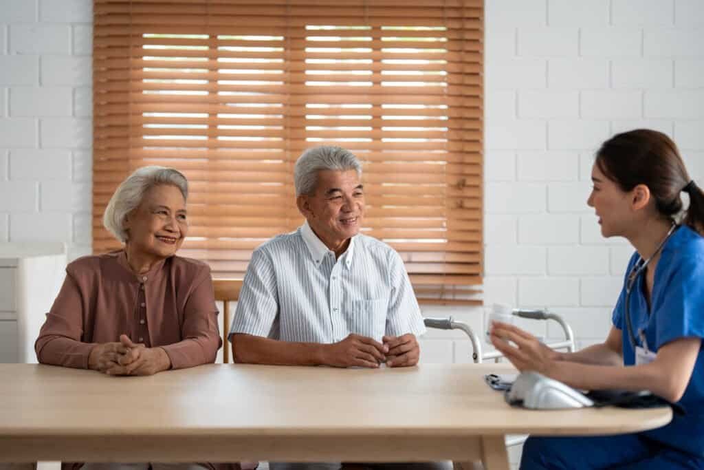 Asian caregiver nurse examine senior man and woman patient at home. Attractive young specialist career female support give advise and consult to older elderly mature couple in living room in house.