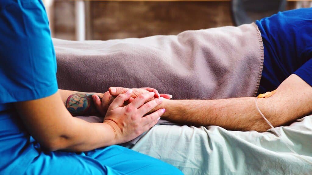 Close up hand touching ill old person in hospital bed