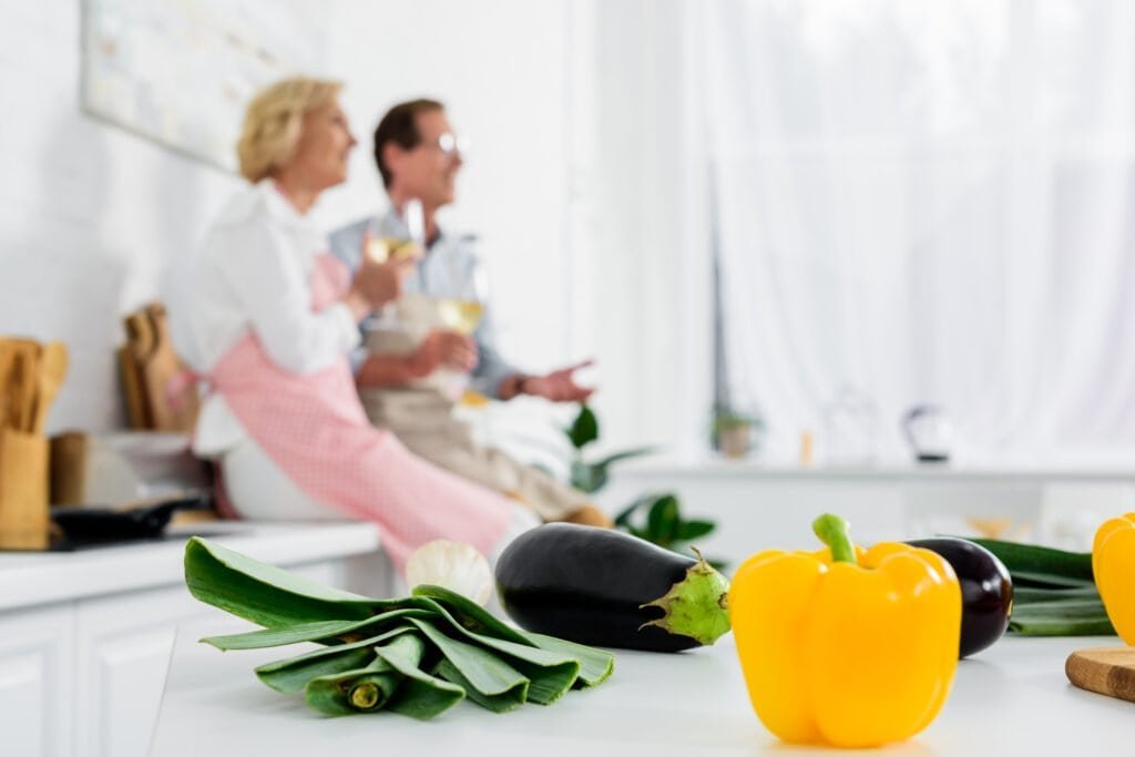 close-up view of fresh vegetables on kitchen table and elderly couplclose-up view of fresh vegetables on kitchen table and elderly couple drinking wine behinde drinking wine behind