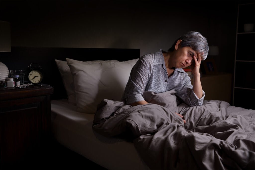 Depressed senior woman sitting in bed cannot sleep from insomnia