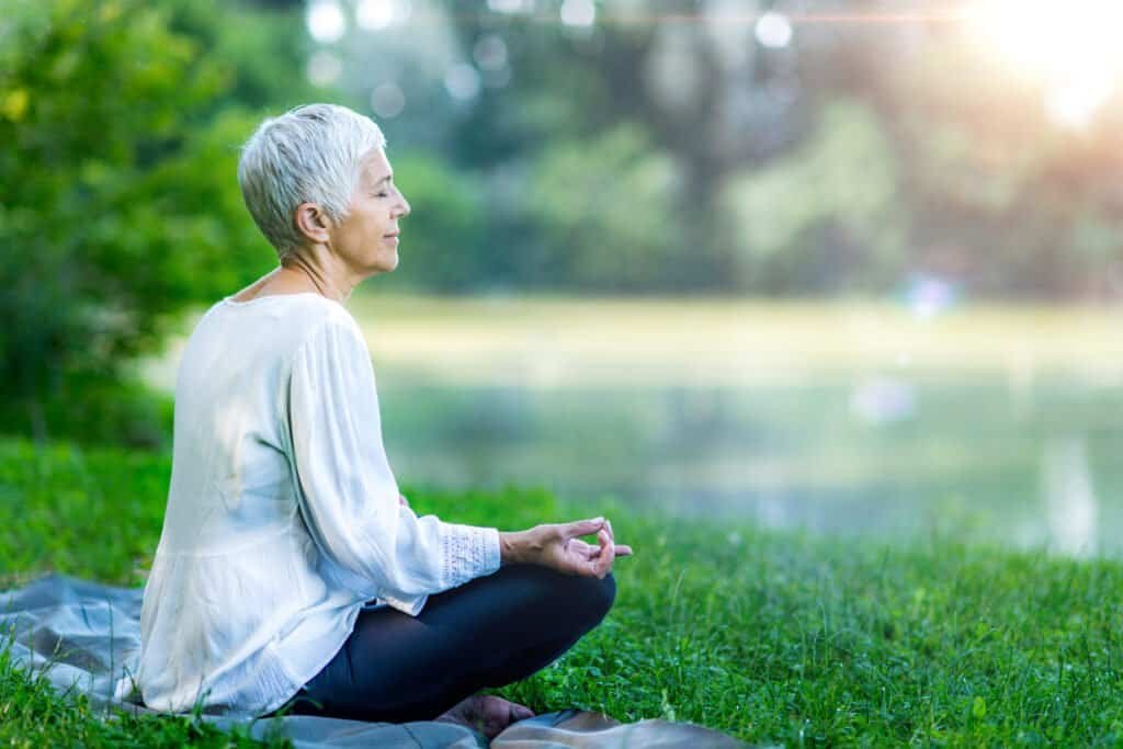 Mindful senior woman meditating by the body of water
