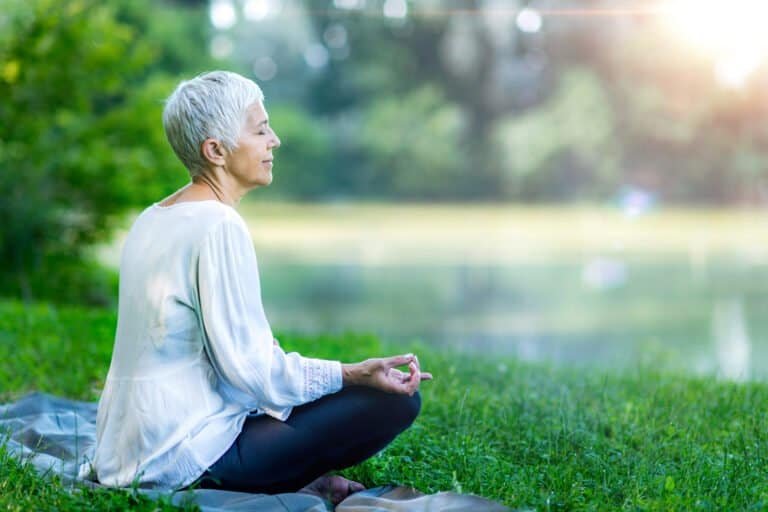 Mindful senior woman meditating by the body of water